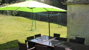 Ein Tisch mit Glasplatte, acht Stühle, ein grüner Sonnenschirm und eine Backsteinmauer im Hintergrund.