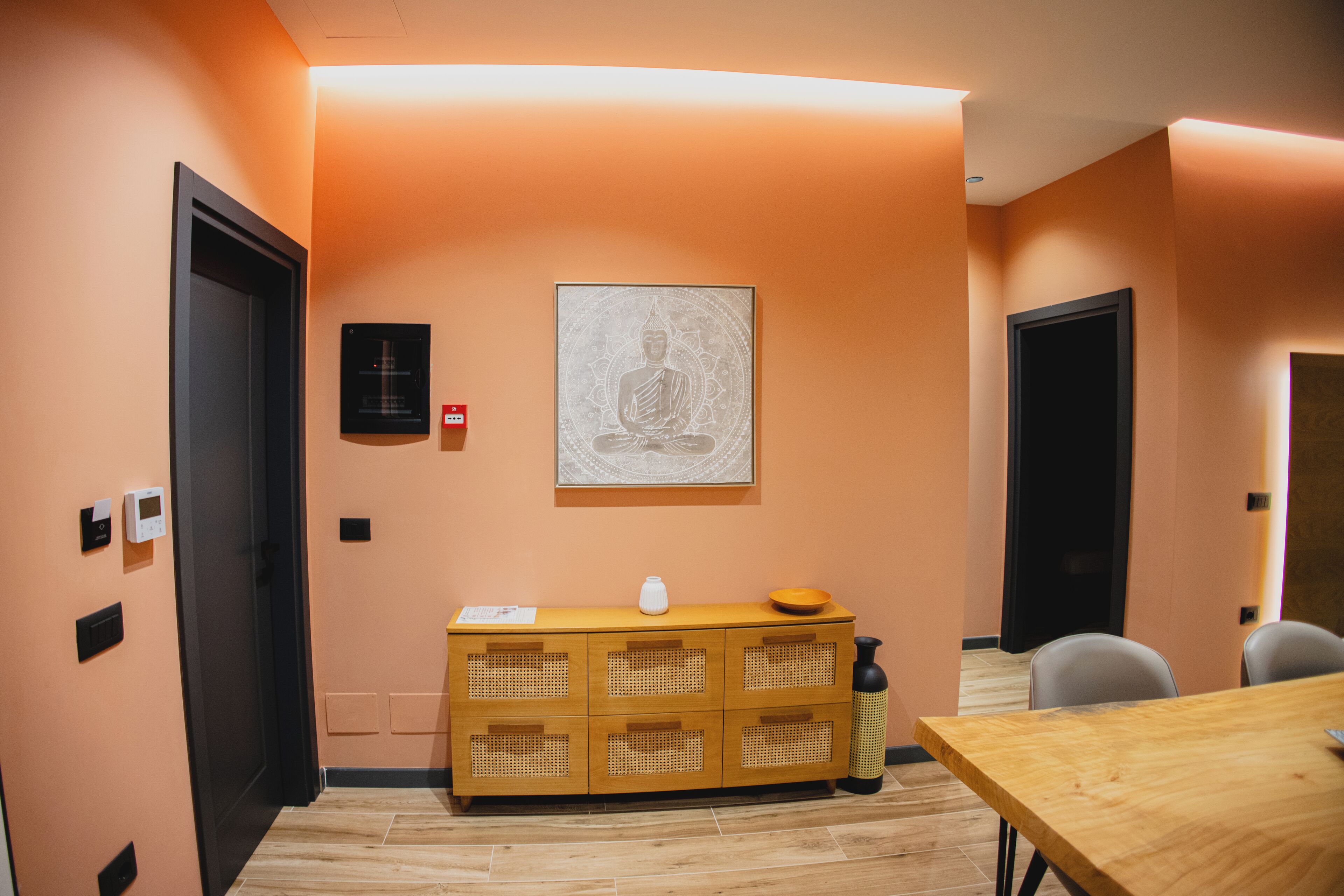 Une salle de conférence avec une table en bois, un meuble contenant une statue de Bouddha et un luminaire fixé au mur.