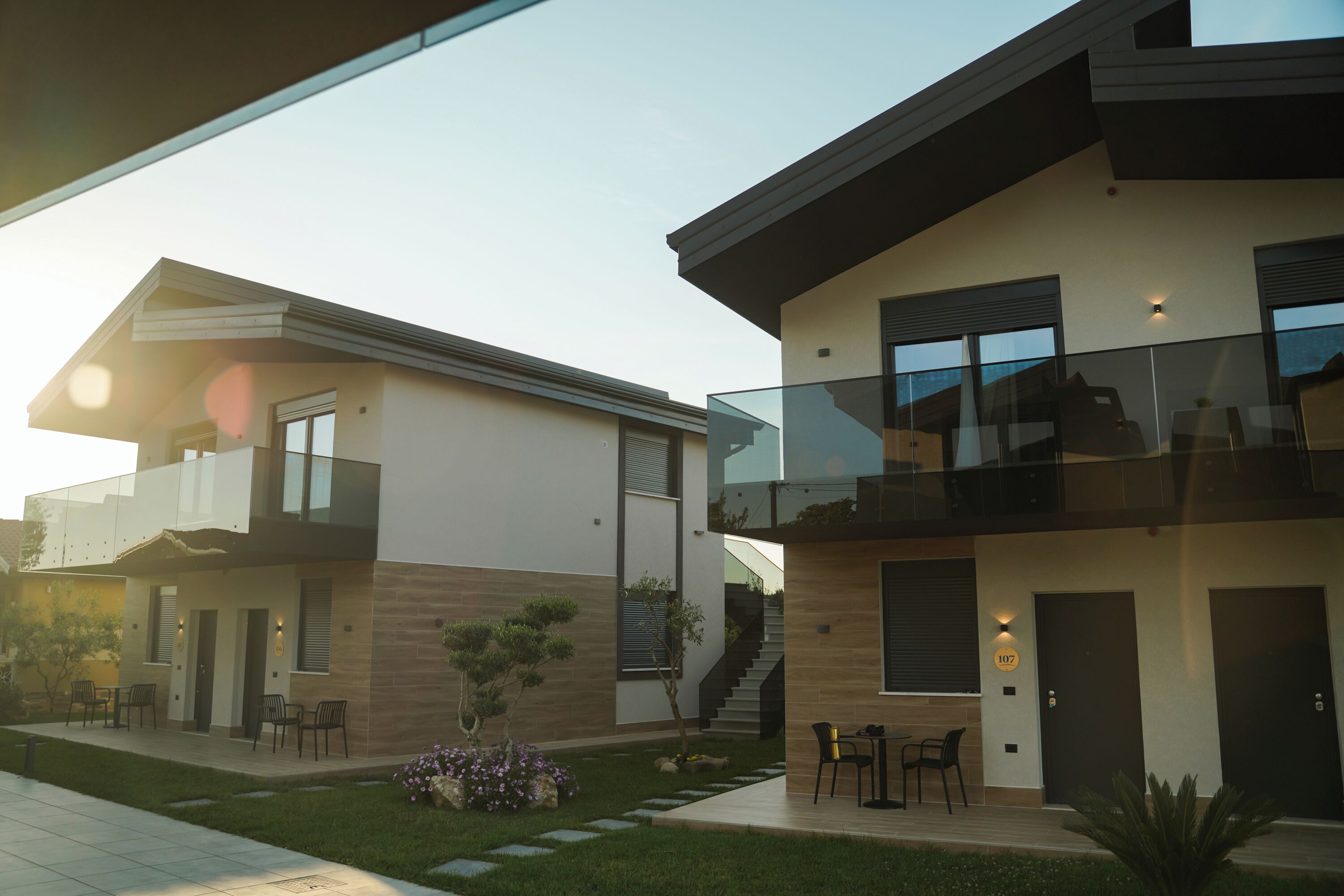 A modern two-story house with a balcony, a staircase, and a small garden area.