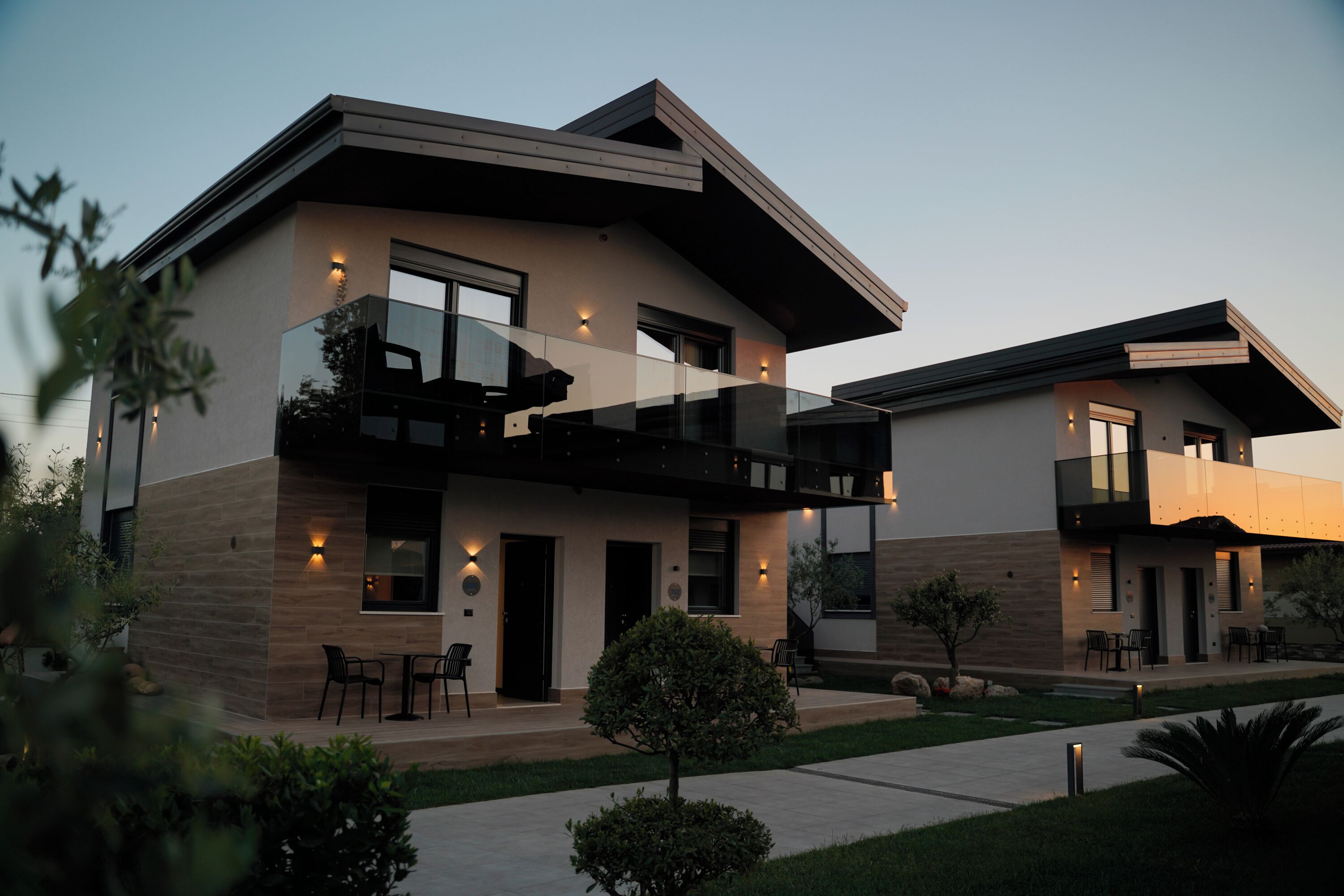 A modern two-story house with a balcony, a small garden, and outdoor seating.