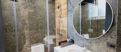 A modern bathroom with a glass shower enclosure, a large round mirror, and a white sink.