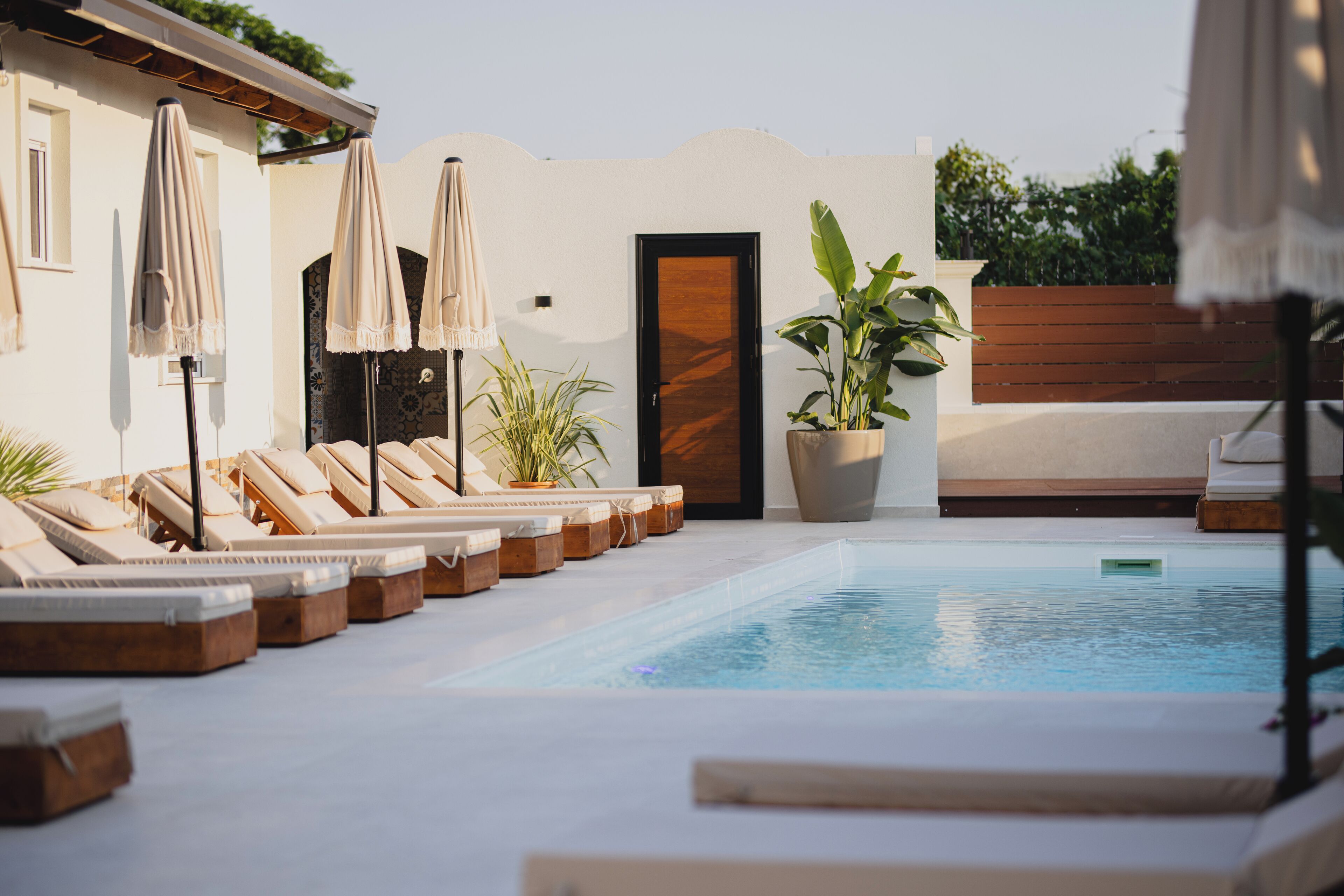 A poolside area with lounge chairs and umbrellas, a wooden door, and potted plants.