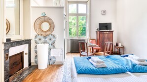 Una habitación de hotel con una cama, una zona de estar con una mesa y sillas, una chimenea, un ventanal con vistas a zonas verdes y un televisor sobre un mueble de madera.