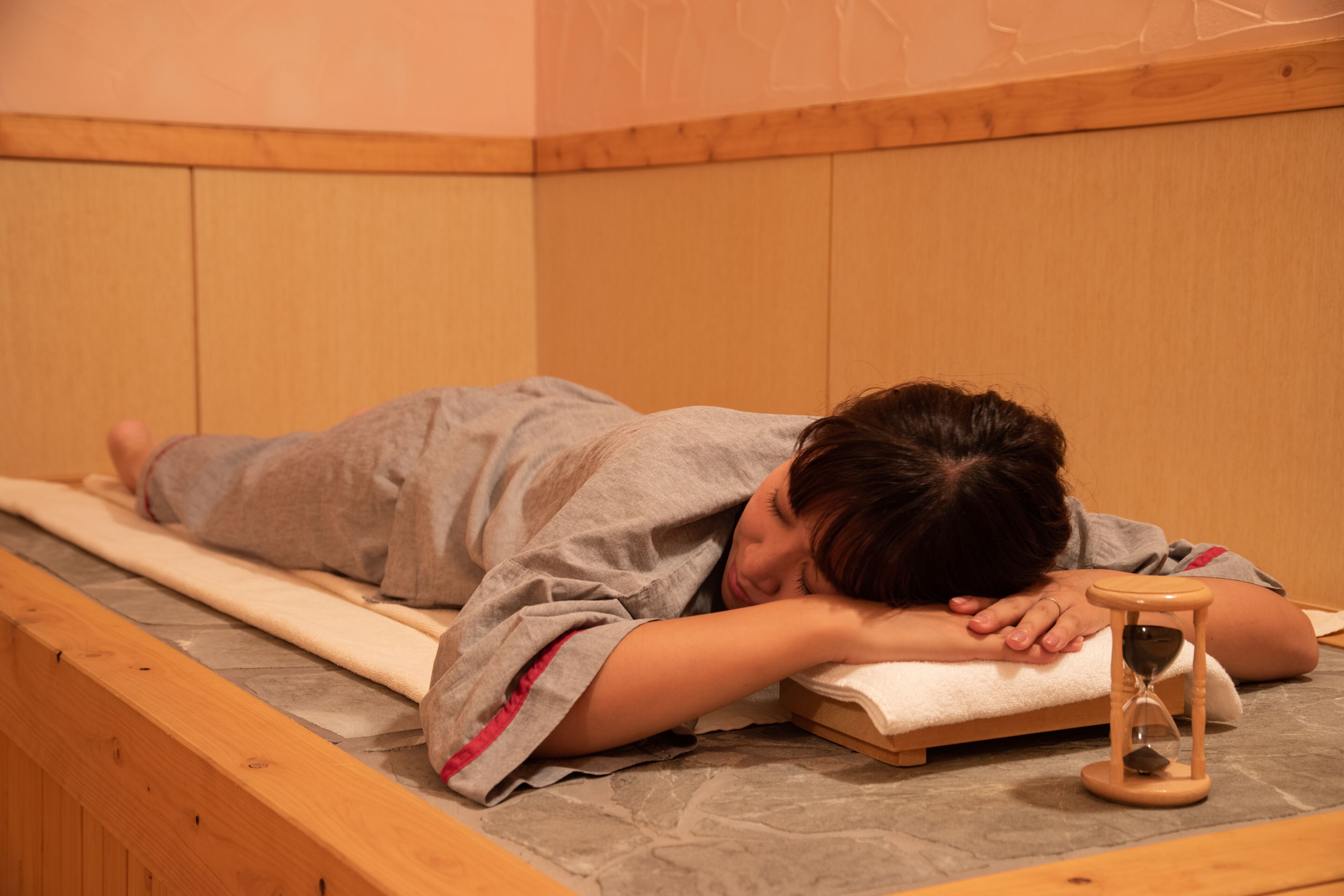 A person lying on a bed in a room with wooden paneling and a small hourglass.