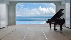 A grand piano in a spacious room with a large window overlooking a body of water. - amafuru-oka (Ibusuki)