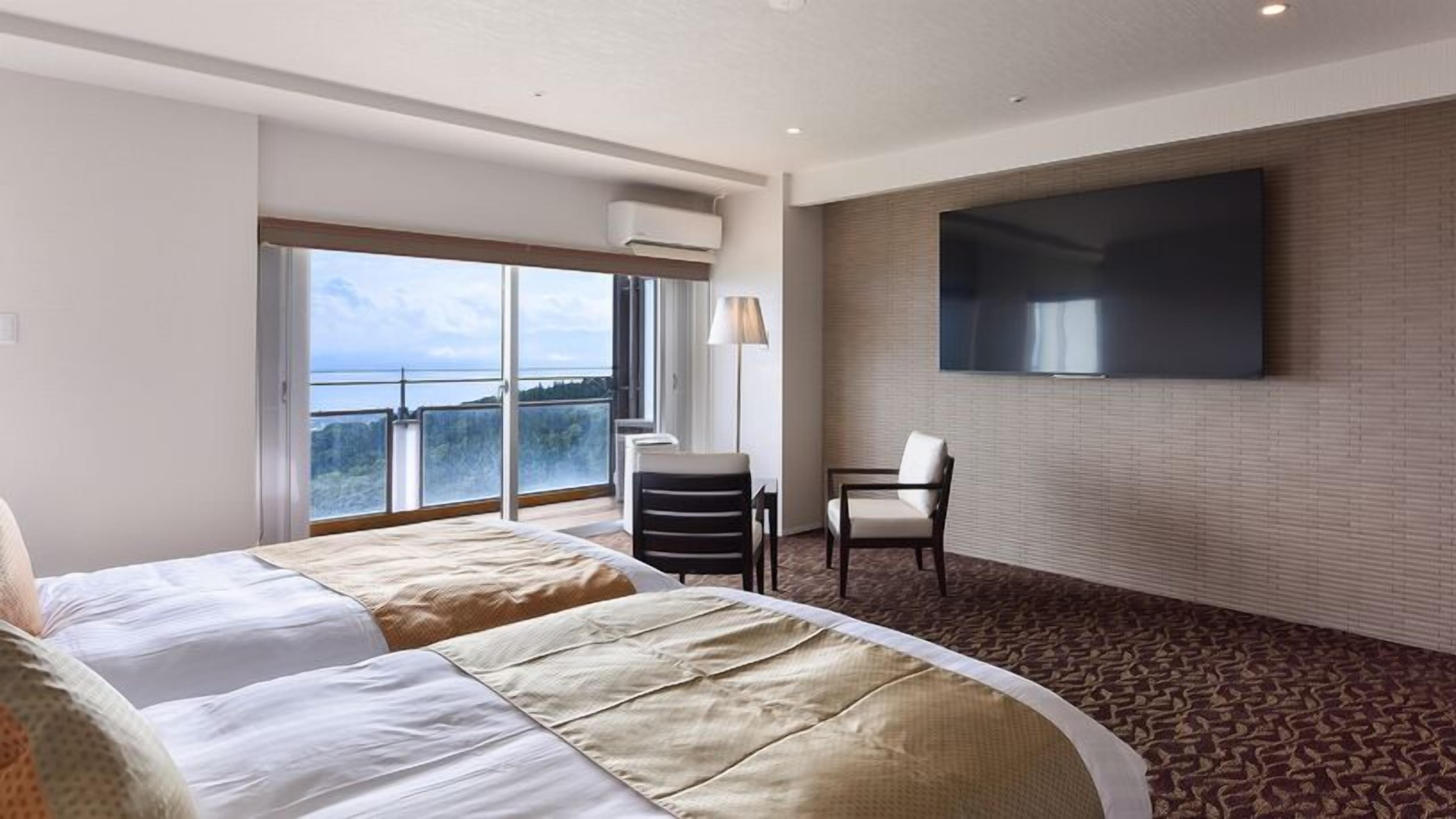 A hotel room with a large bed, a desk, a chair, a TV, and a balcony with a view.