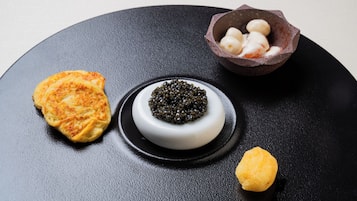 A black plate with three items: a round pastry, a bowl of caviar, and a small yellow item.