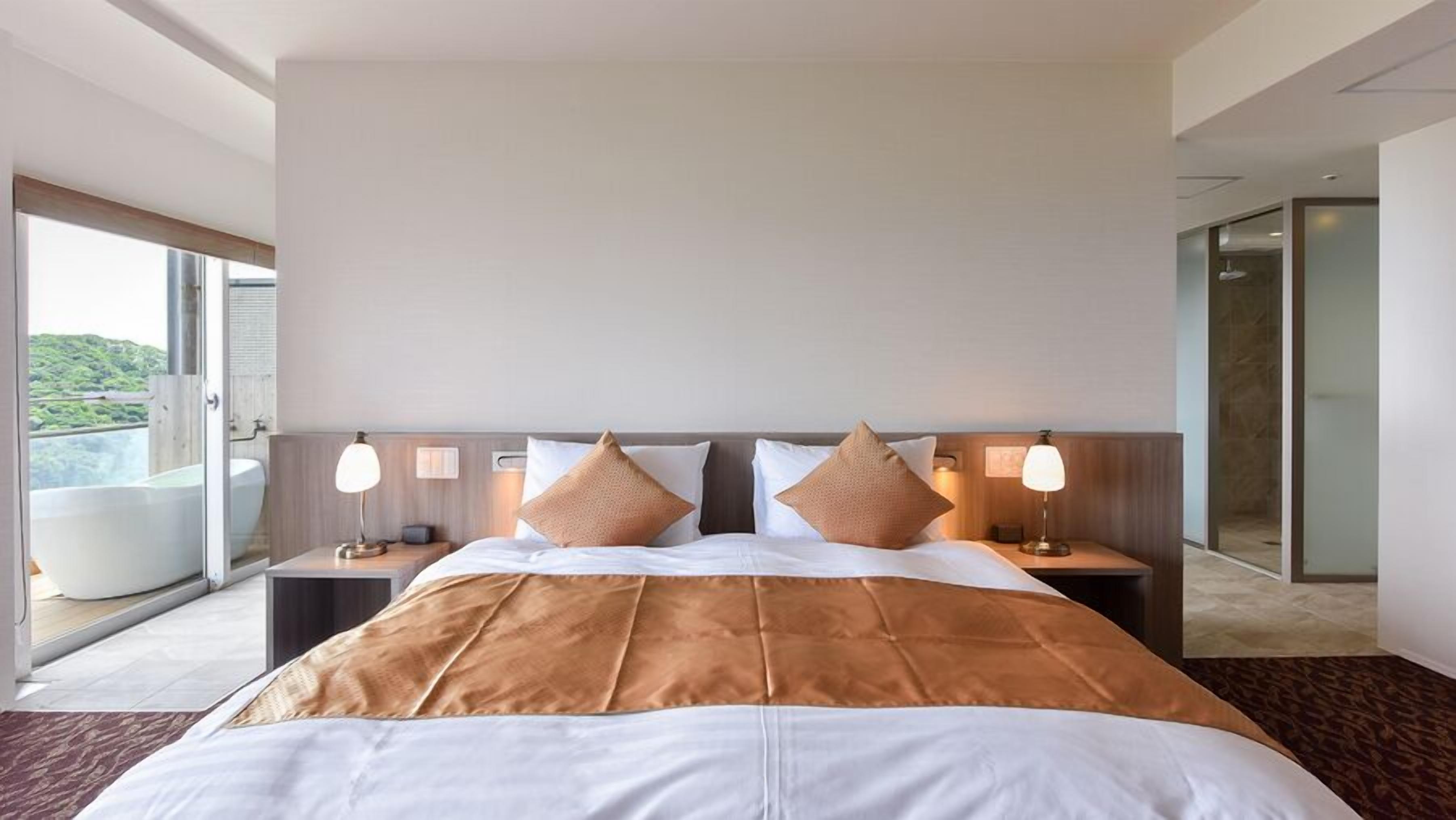 A hotel room with a large bed, two bedside tables, a window with a view, and a bathroom with a shower.
