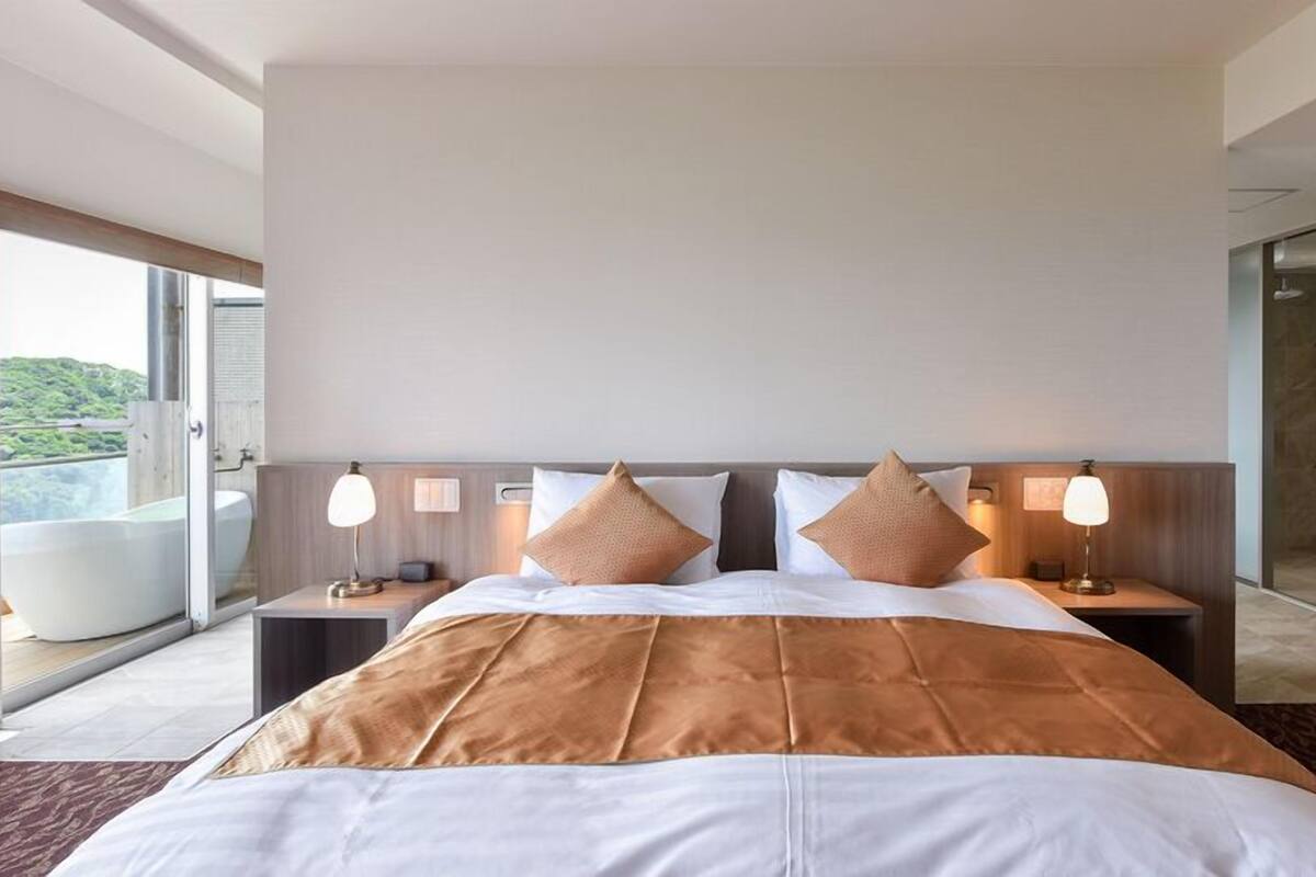 A hotel room with a large bed, two bedside tables, a window with a view, and a bathroom with a shower.