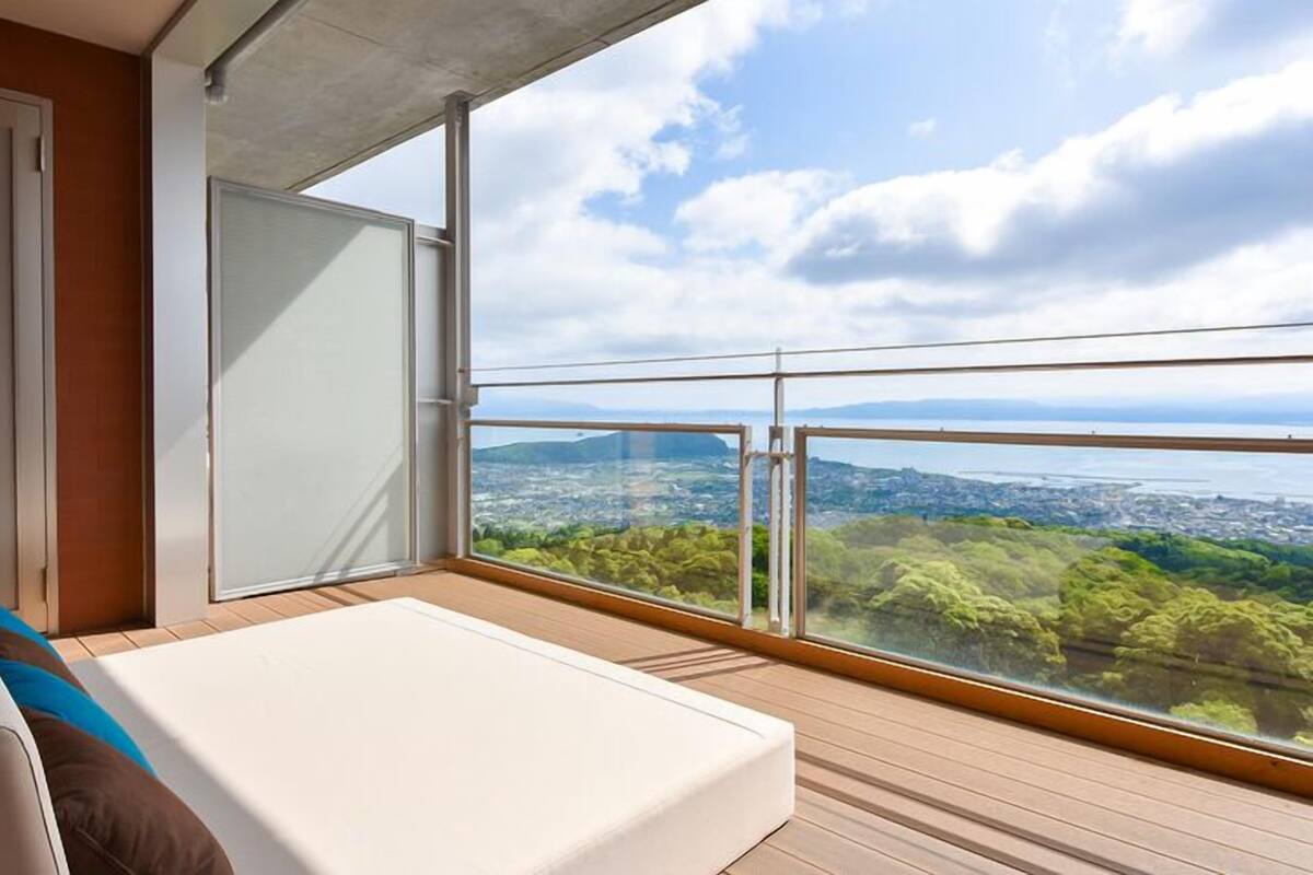A balcony with a bed, a sliding door, and a view of a city and water.