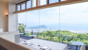 A dining area with a table set for four, overlooking a cityscape with mountains in the distance. - amafuru-oka (Ibusuki)