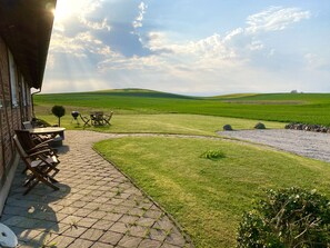 Une terrasse avec des meubles d’extérieur, un chemin de pierres et une vue sur des collines verdoyantes.