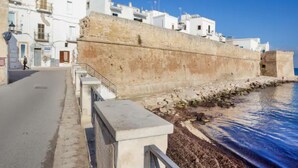 A coastal street with white buildings, a stone wall, and a clear blue sky. - GuestHost - NEW! Apt in the heart of Monopoli! 200m from sea! (Monopoli)