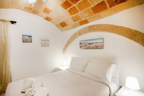 A bedroom with a bed, white linens, a nightstand, a lamp, and three framed pictures on the wall.