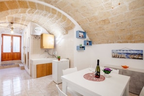 A kitchen with a stone arch, a white countertop, a sink, and a dining area with a table and chairs.