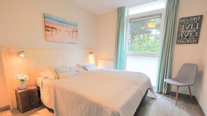 A bedroom with a bed, bedside lamps, a window with curtains, a chair, and a painting on the wall.