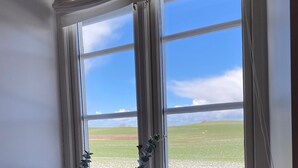 Una habitación con un ventanal que da a un campo, dos jarrones blancos en un repisa y una cortina blanca.