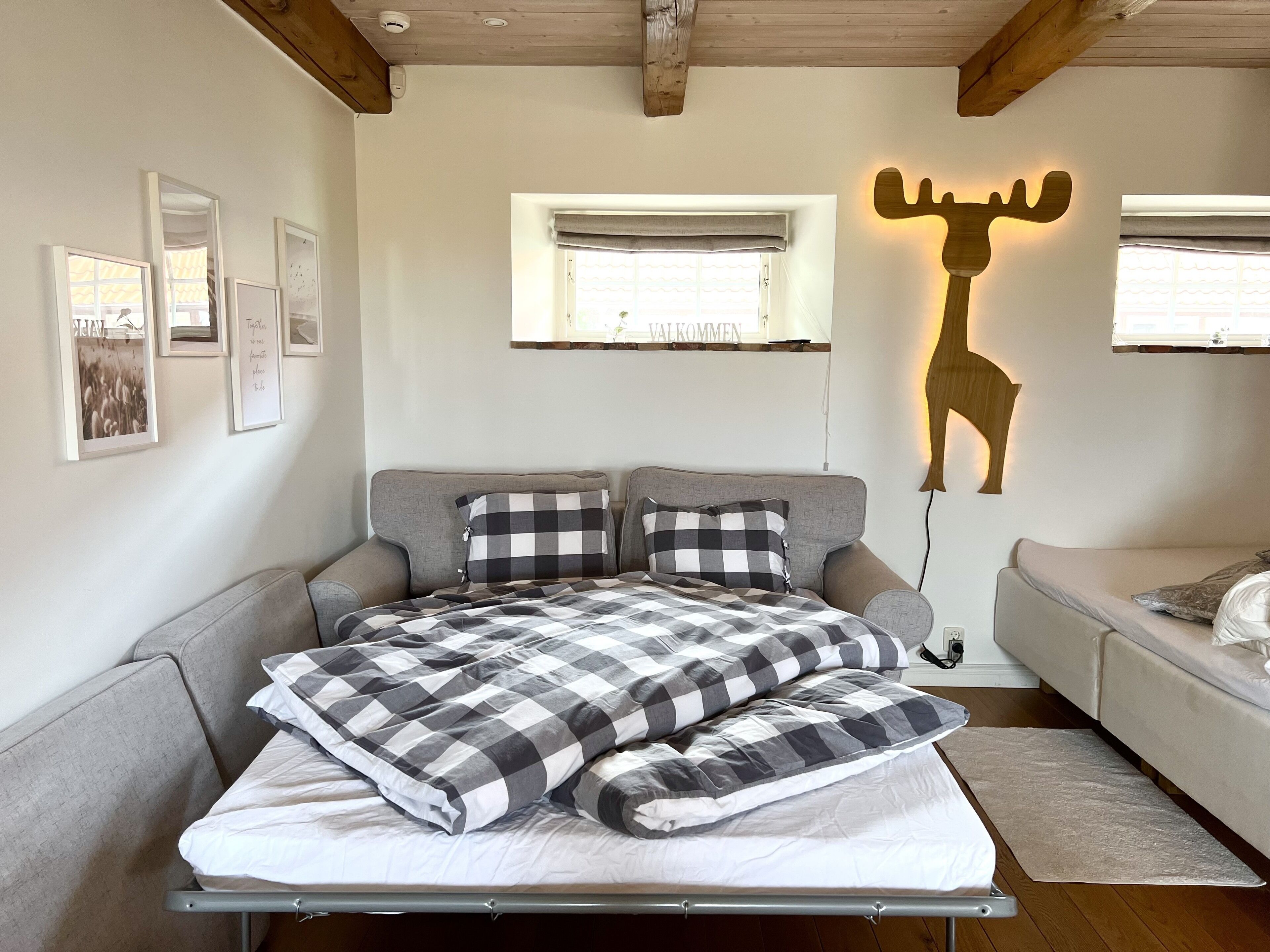 A bedroom with a bed, a sofa, a wall-mounted deer light, and framed pictures.