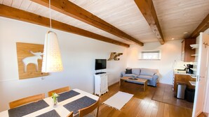 Una sala de estar acogedora con techo de madera, un comedor con mesa y sillas, un sofá, un televisor y una zona de cocina con cafetera.