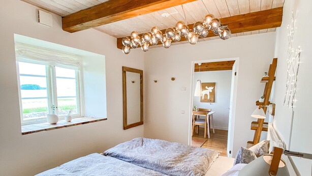 Un dormitorio con techo de madera, una cama con ropa de cama estampada, una lámpara de noche y una ventana con vistas al exterior.