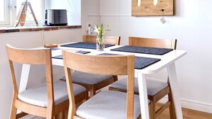 Un comedor con una mesa de madera, cuatro sillas, una lámpara colgante, un silueta de animal enmarcada y una ventana con cortinas.