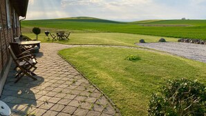 Un patio con mobiliario exterior, un sendero de piedra y vistas a colinas verdes.