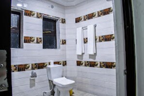 A bathroom with white tiles, a toilet, a sink, and a window with a metal grate. - Wonderland Destination Resort (Naivasha)