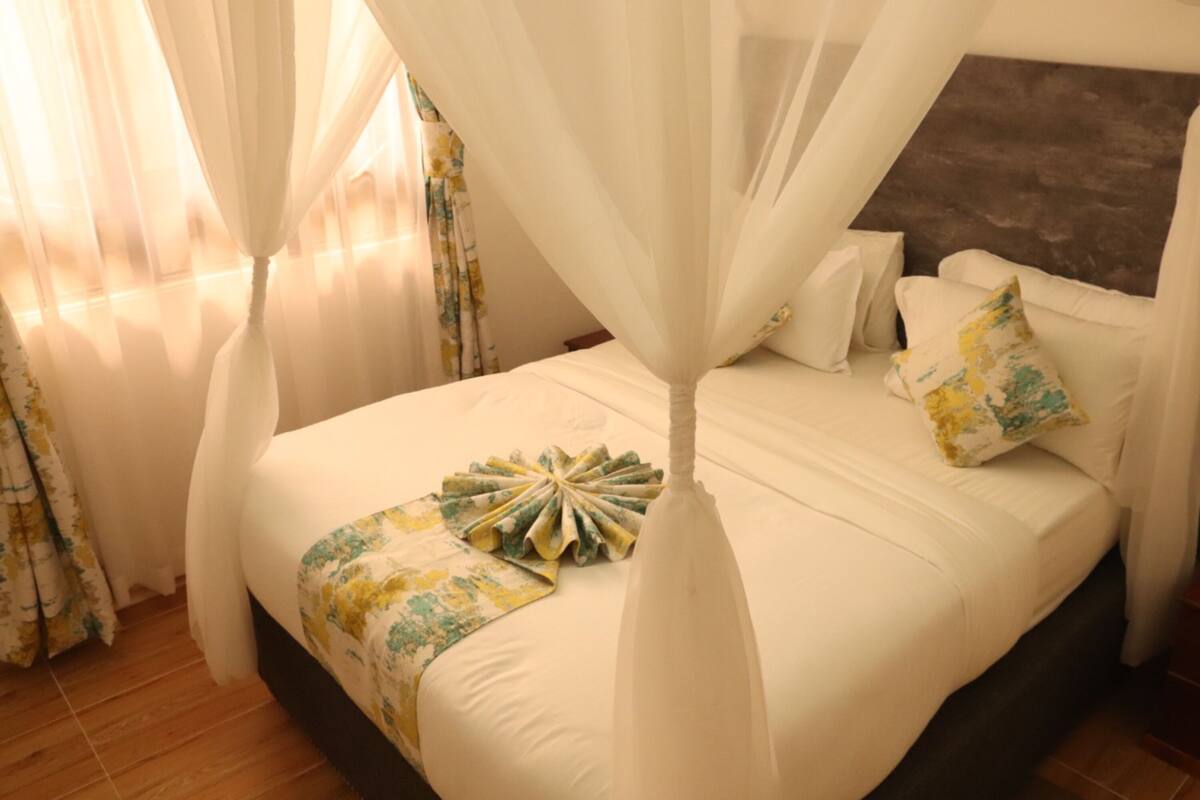 A bed with a canopy, white bedding, and a floral-patterned throw.