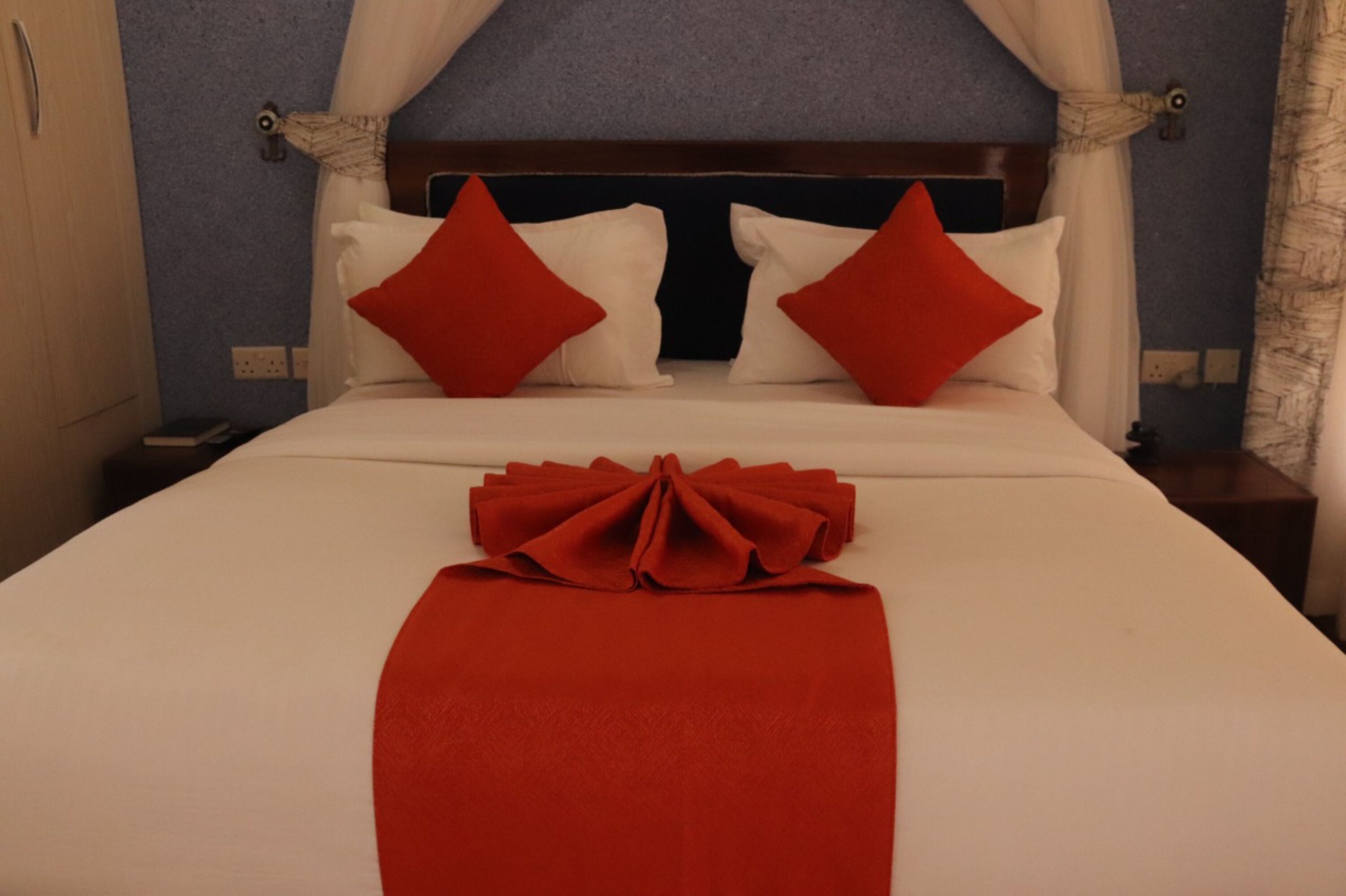 Un letto rifatto con cuscini bianchi e rossi, una coperta rossa e un baldacchino.