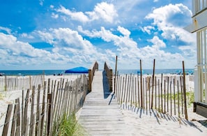 A wooden boardwalk leading to a beach with a clear sky and a distant mountain.