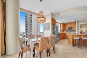 A modern kitchen with a central island, wooden cabinets, and a large window offering a city view.