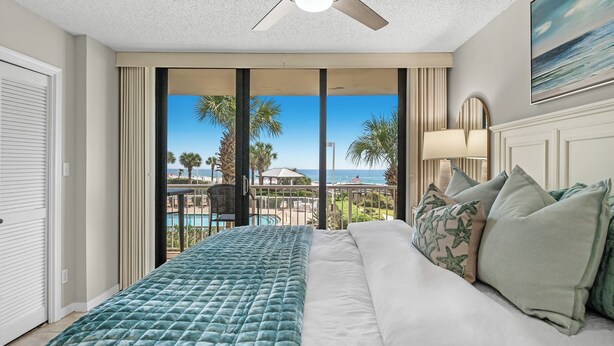 Ein Hotelzimmer mit Bett, Deckenventilator, Blick auf den Strand und Pool.