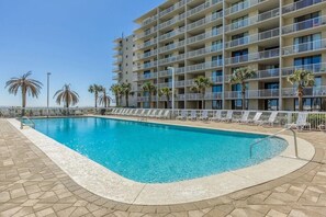 A swimming pool with lounge chairs and palm trees, surrounded by a multi-story building with balconies.