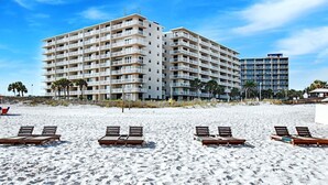 Ein Hotel direkt am Strand mit mehreren Etagen, einem Sandstrand im Vordergrund und Palmen.