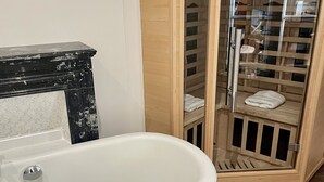 Ein Badezimmer mit freistehender Badewanne, einem Holzwaschtisch, einer gläsernen Dusche und einer digitalen Bedienkonsole.