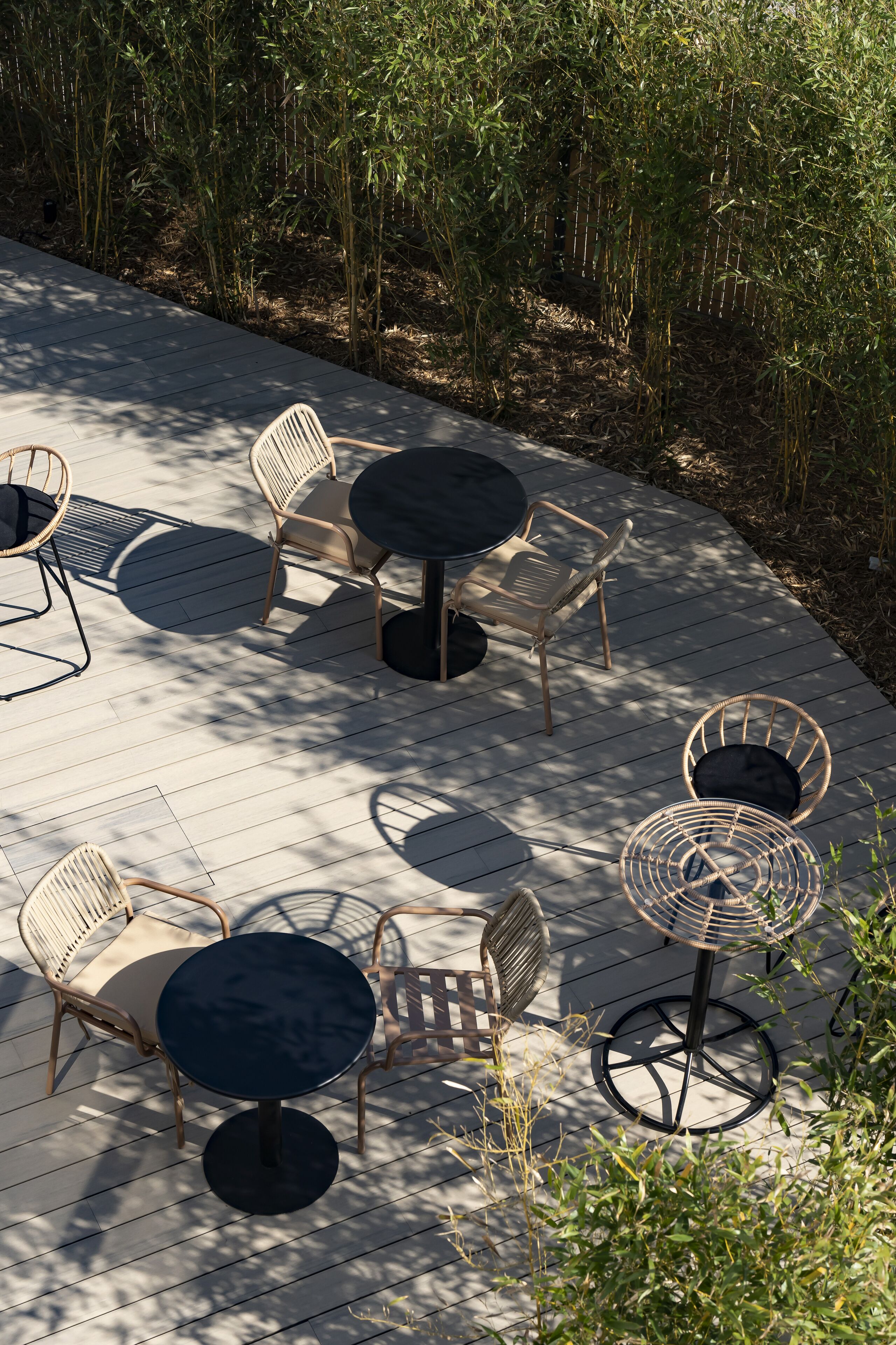 Eine Terrassengaststätte mit runden Tischen und Korbstühlen, umgeben von Bambuspflanzen.