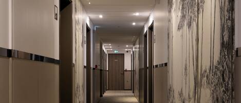 A long, narrow hallway with carpeted floors and doors on both sides leading to rooms.