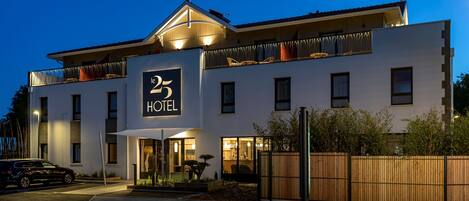 Un hotel moderno con un llamativo letrero que dice '25 HOTEL', ventanas amplias y un balcón con cortinas.