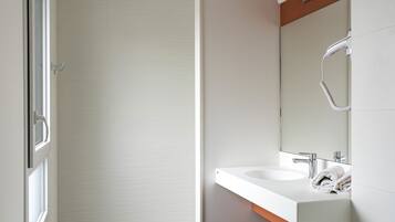 A modern bathroom with a white sink, a mirror, and a shower area.