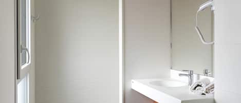 A modern bathroom with a white sink, a mirror, and a shower area.