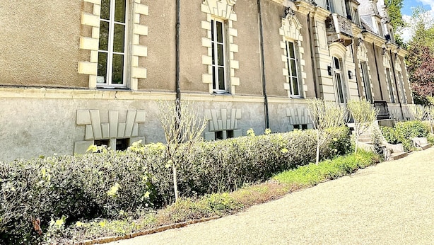 Un edificio histórico de arquitectura simétrica, con amplias ventanas y un jardín bien cuidado.