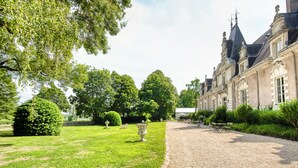 Un jardín formal con un sendero de grava, setos cuidadosamente recortados y un edificio clásico de arquitectura simétrica.