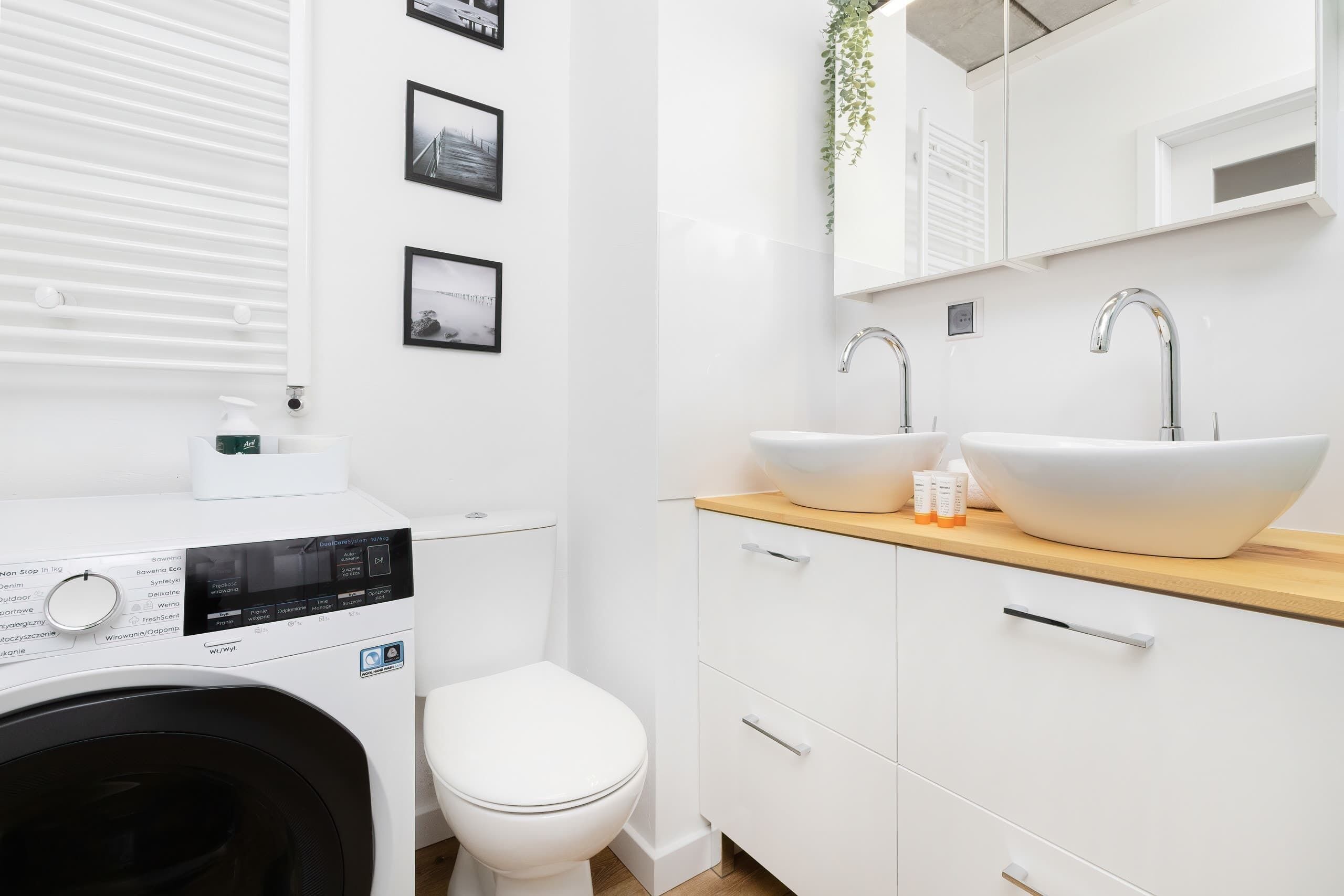 A modern bathroom with a washing machine, two sinks, and a toilet.