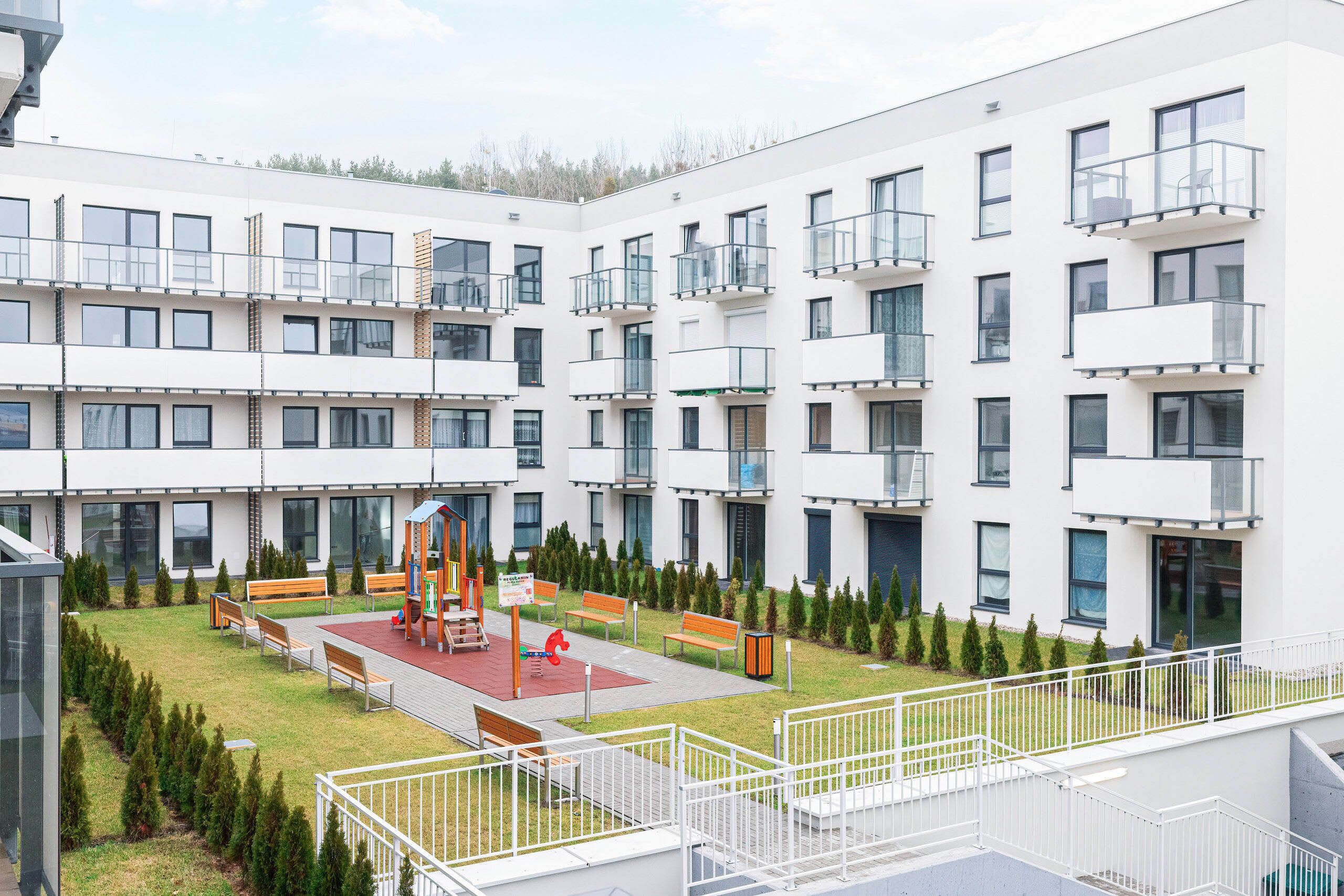 Un moderno edificio de apartamentos con varios balcones, un patio central con bancos y un parque infantil.