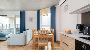 A modern kitchen with a dining area, wooden table, chairs, and a coffee maker. - Spacious Apartment | 3 Bedrooms, Air Conditioning, Parking (Gdynia)