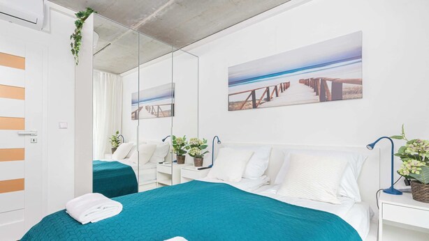 A modern hotel room with a large bed, a mirror, and artwork on the walls. - Spacious Apartment | 3 Bedrooms, Air Conditioning, Parking (Gdynia)