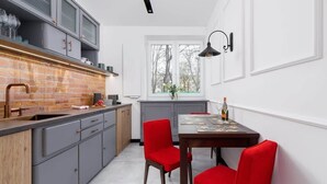 A modern kitchen with grey cabinets, a brick backsplash, and a window overlooking a tree-lined street. - Apartment in a green area | Workspace (Kraków)