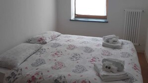A bedroom with a bed, a window with a blue curtain, and a radiator. - Downtown apartment, pets allowed (Paularo)