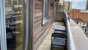 A balcony with a view of a cityscape, featuring a wooden exterior wall, a metal railing, and a table with chairs.