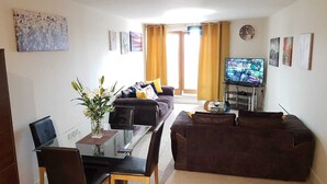 A living room with a sofa, a TV, a coffee table, and a dining area with a table and chairs.